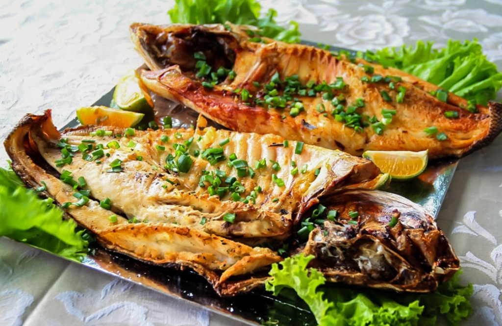 Prato de peixe assado e grelhado, decorado com cebolinha verde, fatias de limão e folhas de alface.